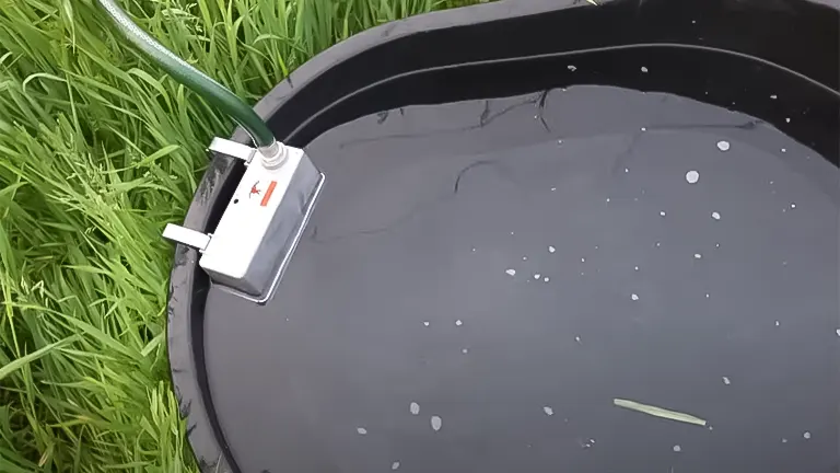 A hose filling a black livestock water trough in a grassy field