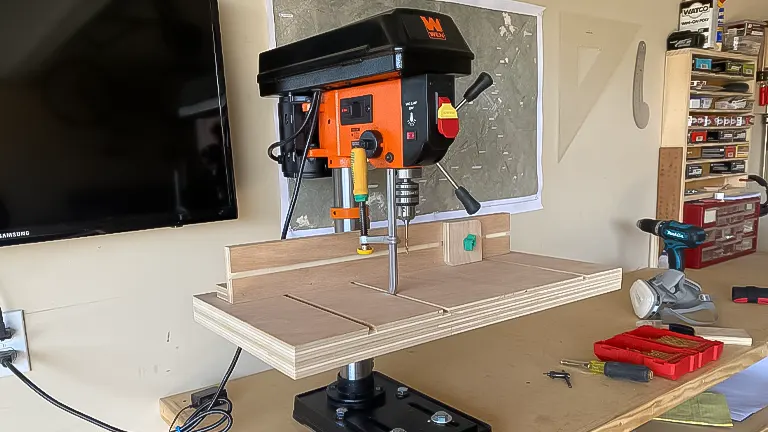 A WEN drill press in use on a plywood workbench, with tools and a TV in the background