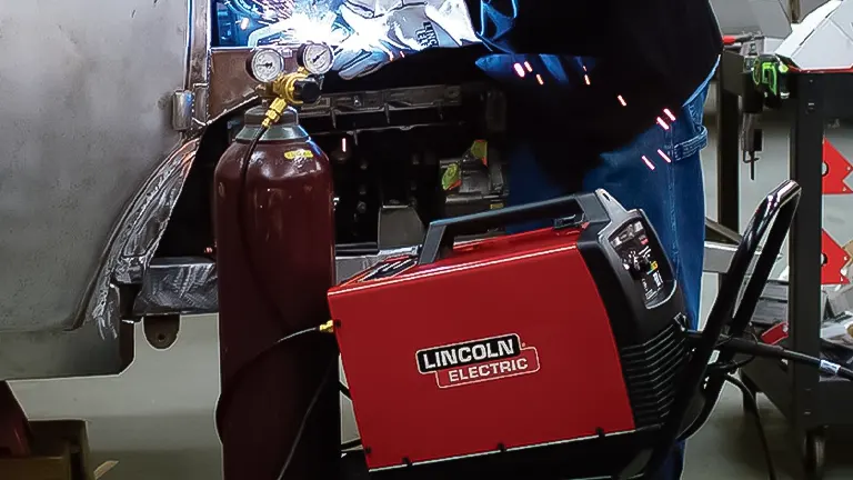 Person using a Lincoln Electric welder with a gas cylinder in the background