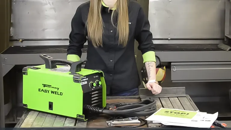 Person presenting a Forney Easy Weld 140 FC-i welder on a workbench