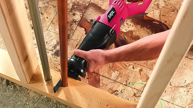 Hand operating a pink SKIL reciprocating saw to cut through a wooden beam