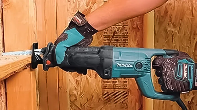 Hand wearing a glove operating a blue and black Makita reciprocating saw through wood