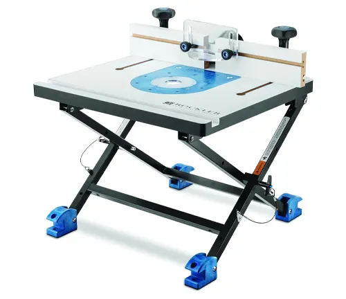 A compact and foldable benchtop router table with an adjustable fence and a white surface, set on a scissor stand for stability