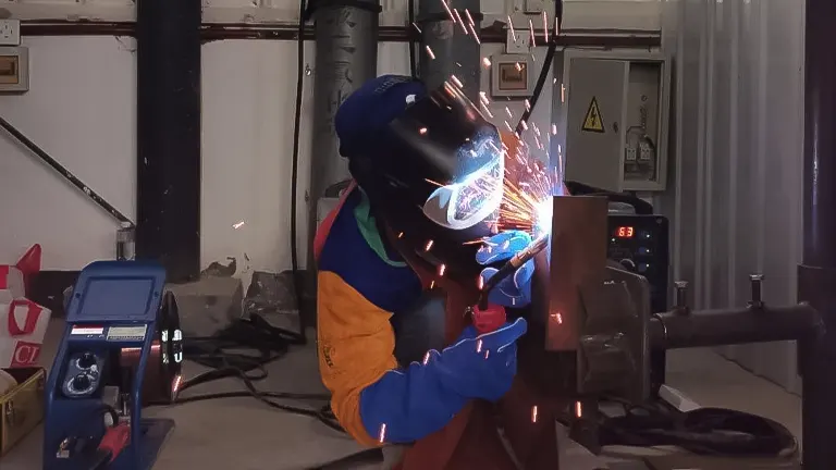 A welder in protective gear using a stick welder on metal with sparks flying