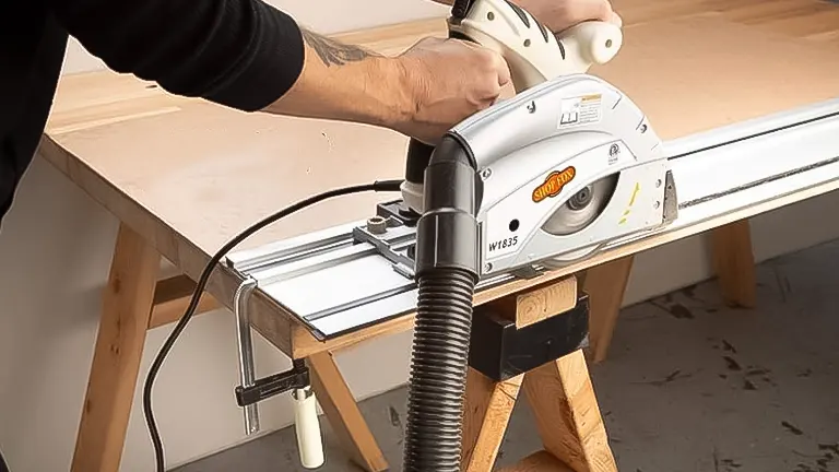Person using a Shop Fox W1835 track saw on a wooden plank with a dust extraction hose attached
