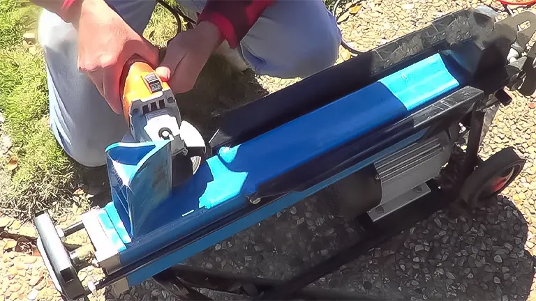 Close-up of a person's hands adjusting a blue log splitter's wedge