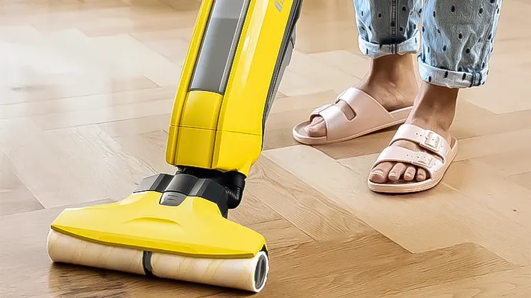 Yellow upright floor cleaner machine in use on a hardwood floor, with a person's feet visible
