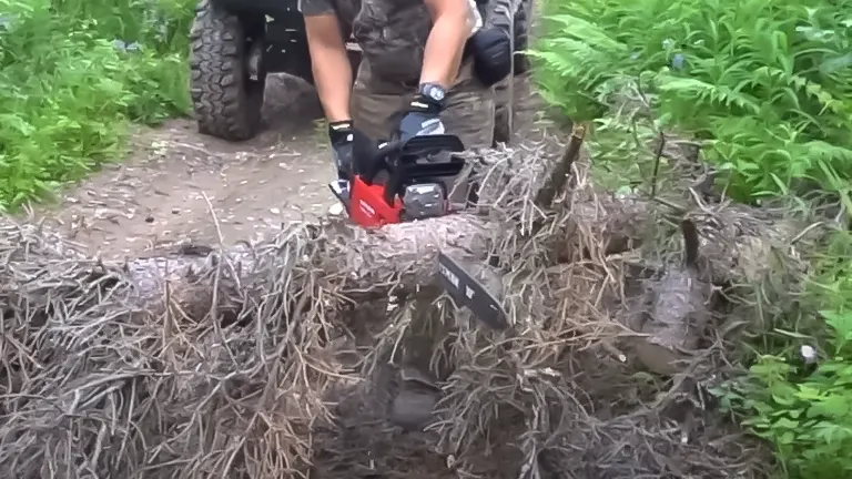 Individual using a CRAFTSMAN S165 chainsaw on a fallen tree, with off-road vehicle tires partially visible