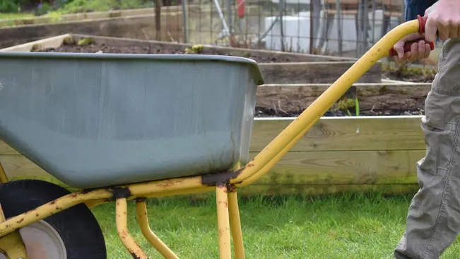 Person gripping the ergonomic yellow handles of a wheelbarrow, showcasing the ease of handling in a garden setting.