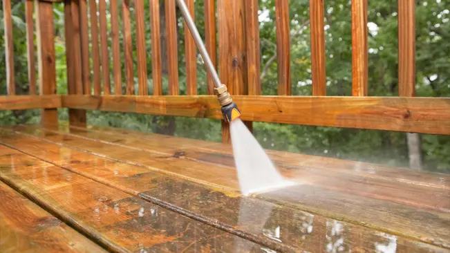 Close-up of pressure washing a wooden deck railing with a high-pressure nozzle.
