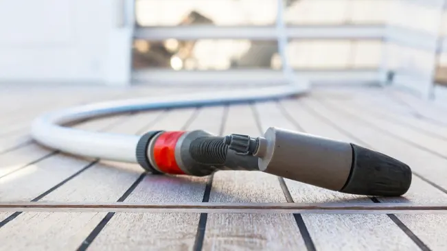 Pressure washer nozzle and hose lying on a wooden deck, ready for use.