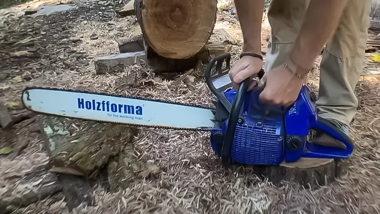 Close-up of a person holding the Farmertec Holzfforma G660 Blue Thunder chainsaw near a log on the ground