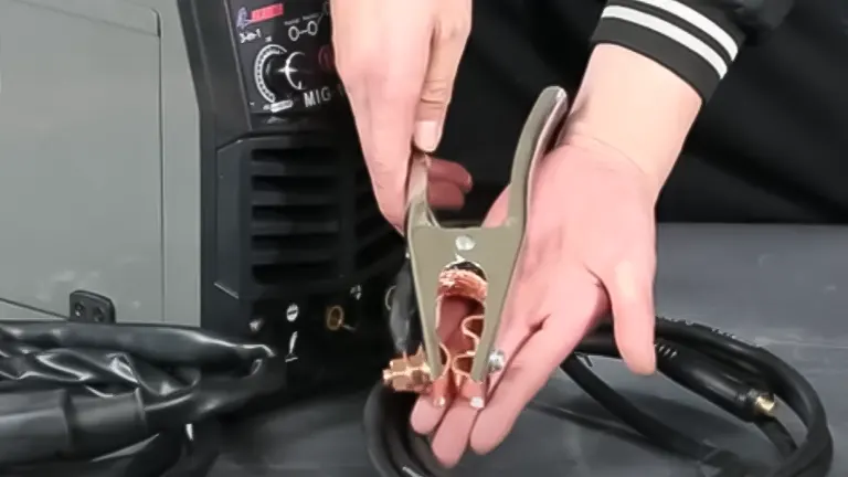 Hands attaching a grounding clamp to a GZ GUOZHI 140Amp Multi-Process Welding Machine
