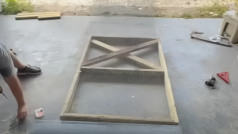 A wooden chicken coop door with hardware cloth being constructed on the ground