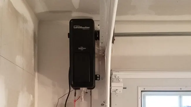 Side view of a wall-mounted LiftMaster garage door operator installed in a white garage interior, with visible wiring and door track components