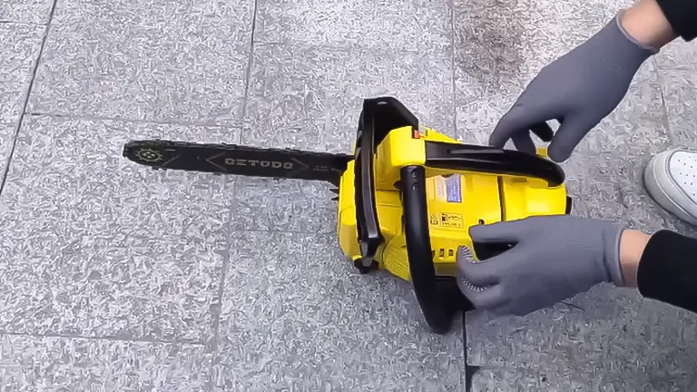 Hands in grey gloves maintaining a yellow and black QZTODO 25.4CC gas-powered chainsaw on a textured floor