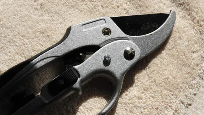 Close-up of a closed ratchet pruning shear on a fabric surface.