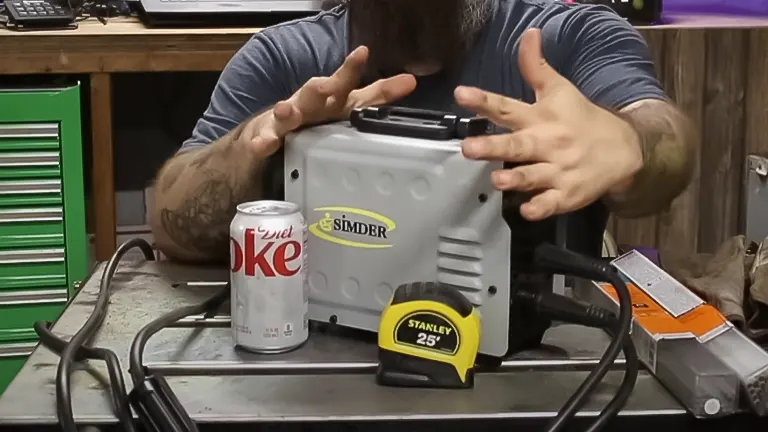 Person presenting SSIMDER Mini ARC200 welder next to a can of Diet Coke and a Stanley tape measure on a workbench