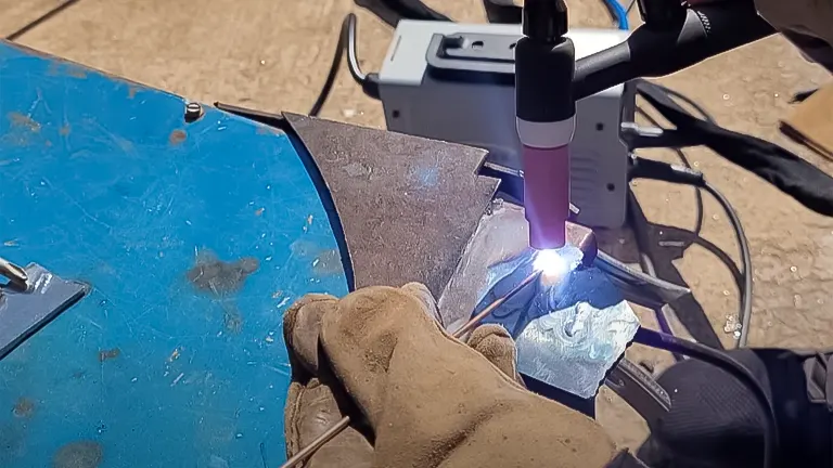 Hand in a protective glove performing TIG welding on metal pieces