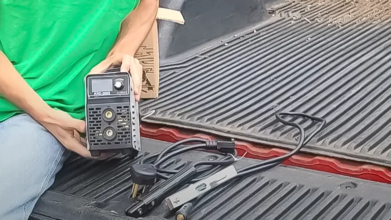 Person holding a SSIMDER Mini ARC200S welder on a truck bed, with cables and welding clamp