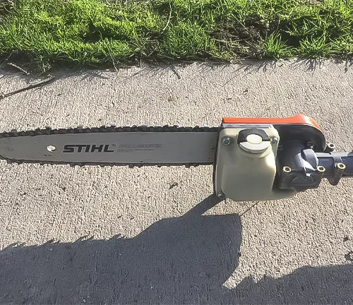 STIHL HT 101 pole saw lying on pavement with the cutting chain and blade visible, next to grass