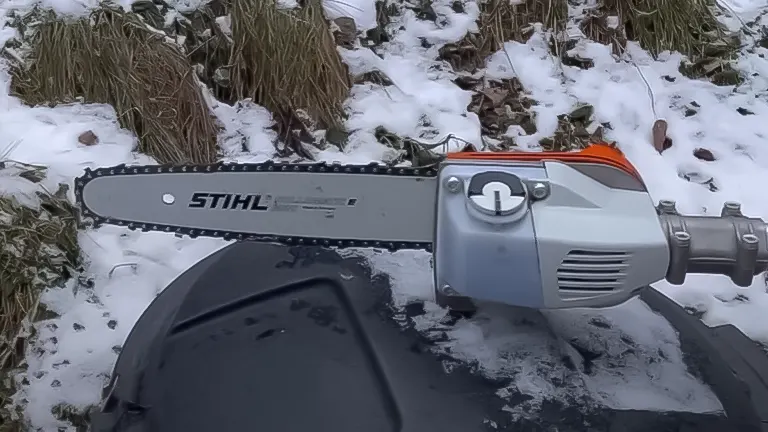 Close-up of the cutting head and chain of a STIHL HT 135 pole saw resting on snow-covered ground