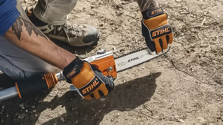 Person in gloves adjusting a STIHL HT 135 pole saw on the ground