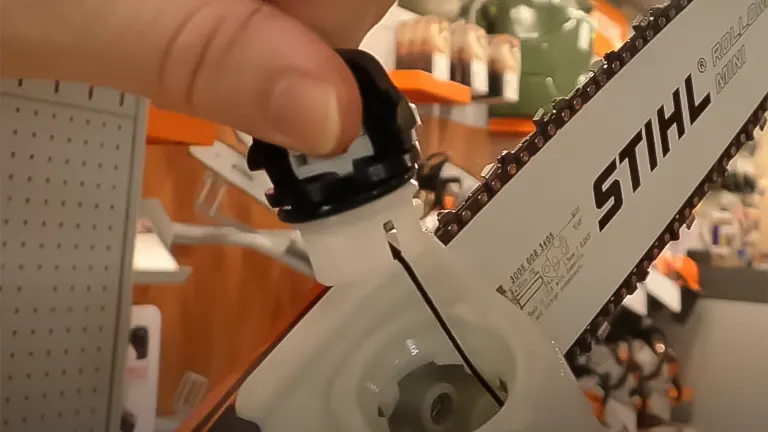 A person's hand opening the oil cap on a Stihl HTE 60 pole saw chain