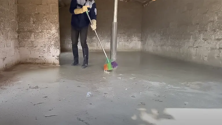 Person cleaning a chicken coop with a broom