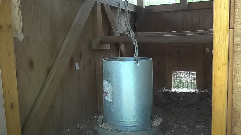 Metal chicken feeder suspended in a coop with a wooden roost