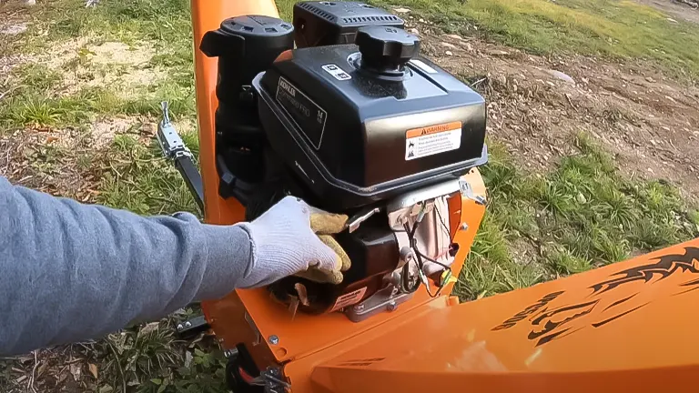Operator starting the engine of a DK2 OPC566E gas-powered wood chipper, showcasing the machine's orange body and black engine