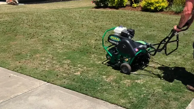 A person operating a green ‘RYAN’ lawn aerator on a well-maintained grassy yard
