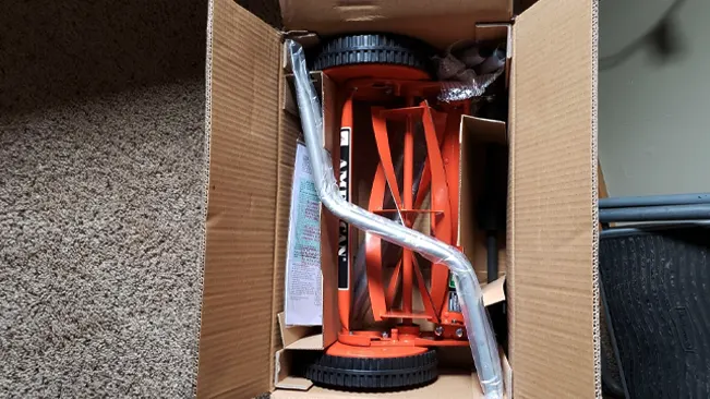 Disassembled orange hand truck in an open cardboard box on a carpeted floor