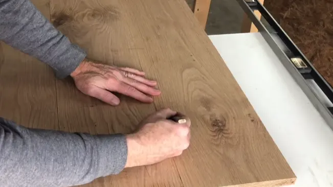Person marking a wooden board with a pencil.