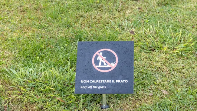 Keep off the grass” sign in Italian and English on a lush green lawn