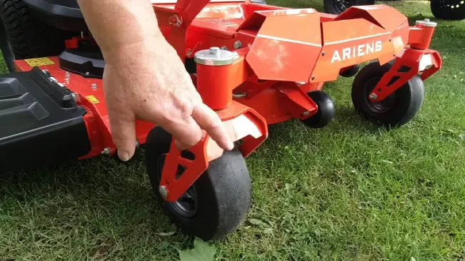 Person inspecting wheels of zero-turn lawn mower.