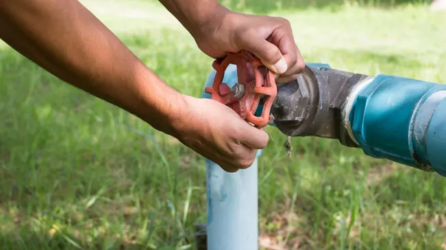 Person turning a red valve on a blue pipeline outdoors