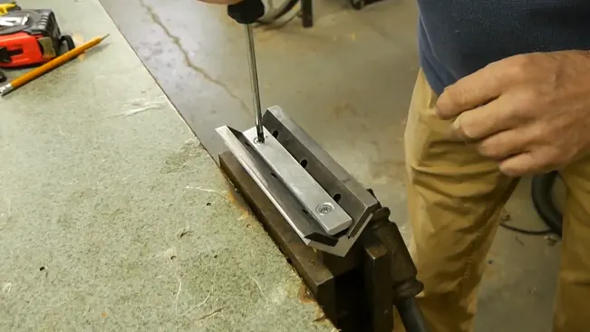 Person using a screwdriver on a clamped metal piece with tools around