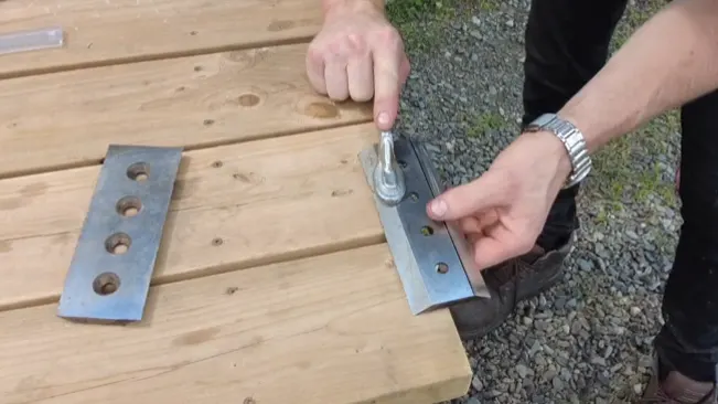 Person tightening nuts on a metal plate on wooden planks