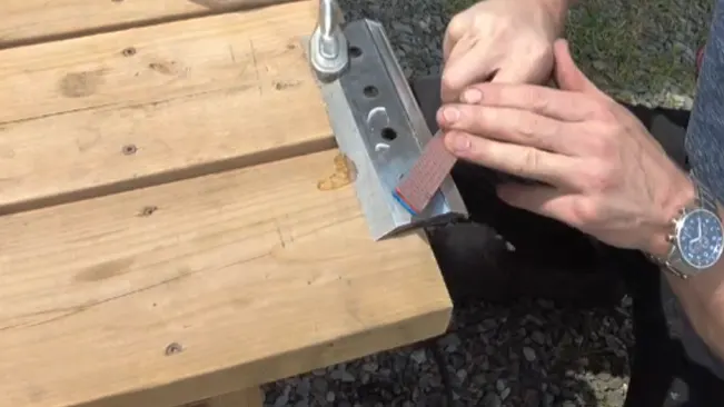 Person Sharpening a metal bracket to wooden planks outdoors