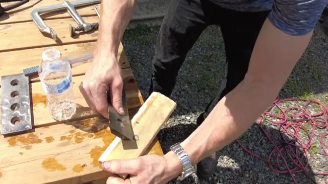 Person sharpening a blade on a wooden block outdoors