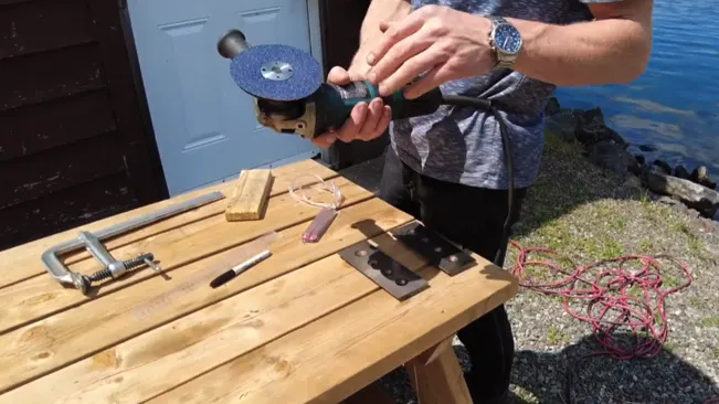 Person sharpening tool on outdoor table with tools and equipment near water