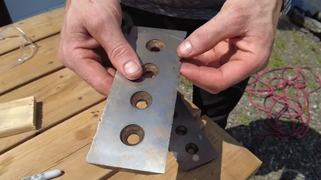 Person holding a metal bracket with holes, with similar object and cables in the background.