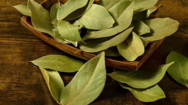 Dried bay leaves in a wooden bowl on a rustic table, essential for flavoring dishes.