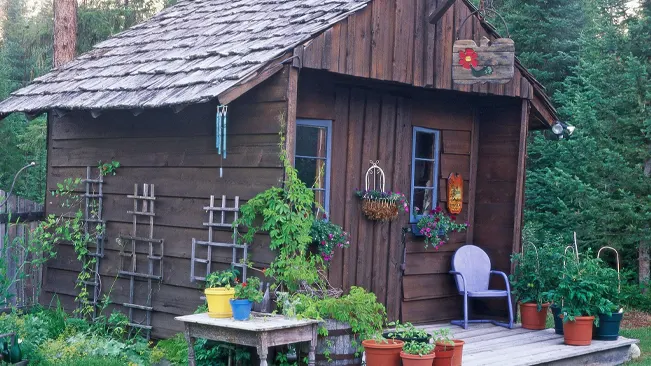 Rustic wooden garden shed with potted plants and gardening tools.
