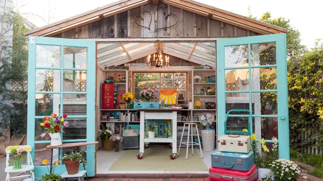 Colorful artist's studio shed with open turquoise doors and creative interior.