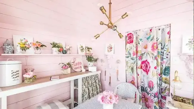 Floral and feminine chic she-shed interior with decorative touches and pastel pink walls.