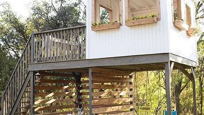 Elevated two-story white garden shed with a wooden balcony.