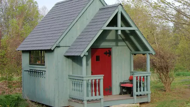 Tudor style garden shed with red door and front porch.