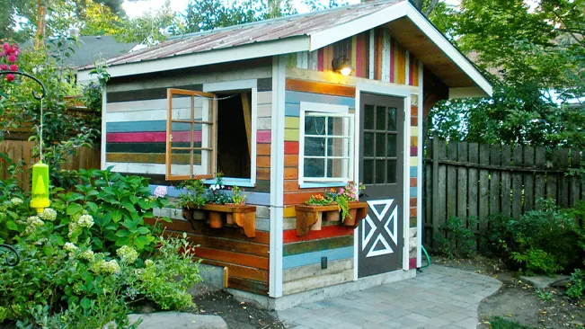 Colorfully painted garden shed with open window and flower boxes.